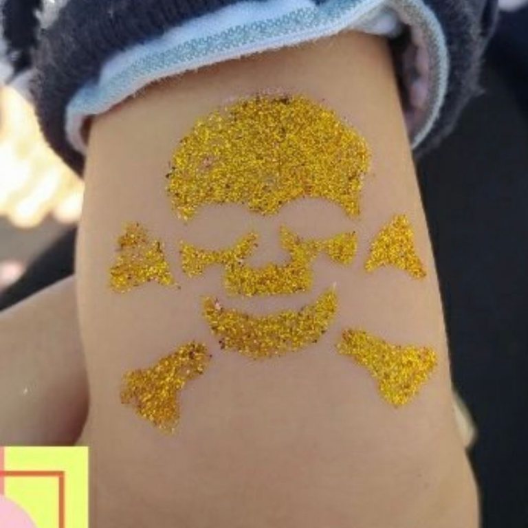 Tatuaje temporal con purpurina dorada de calavera pirata en el brazo de un niño